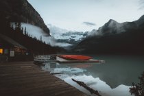 Casa de madera en embarcadero con barcos en el tranquilo lago de montaña - foto de stock