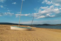 Small vessel placed on sandy shore at lake in sunny day. — Stock Photo