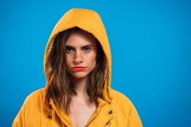 Nachdenkliche Frau mit gelber Kapuze posiert vor blauem Hintergrund — Stockfoto