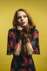 Portrait of redhead woman holding hair and looking at camera on yellow background. — Stock Photo