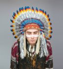 Portrait of man with painted white line on face posing in traditional Native American costume with eyes closed — Stock Photo