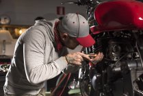 Вид збоку механіка в капелюсі ремонт нестандартного мотоцикла в майстерні — стокове фото