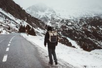 Vue arrière de l'homme marchant sur une route enneigée à la montagne — Photo de stock