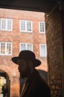 Stylish bearded man in hat leaning on wall at archway — Stock Photo