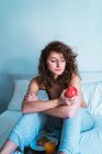 Mujer soñadora sentada con manzana en la cama y mirando a casa . - foto de stock