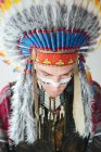 Человек с чертой на лице, позирующий в костюме коренного американца и смотрящий вниз — стоковое фото