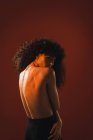 Topless curly woman on red background looking at camera over shoulder — Stock Photo