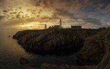 Далекий вид на прибрежную скалу с маяком над закатным небом — стоковое фото