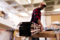 Carpintero borroso llevando piezas de madera apiladas en el taller - foto de stock