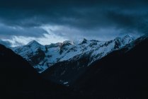View to mountains covered with snow under cloudy heavy sky. — Stock Photo