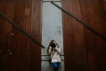 Redhead woman  leaning on wall while focusing with camera. — Stock Photo