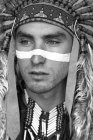 Portrait of man with white line on face wearing Native American costume and looking aside — Stock Photo