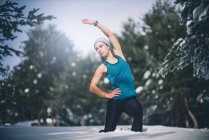 Portrait of fit woman standing in snow and bending aside to warm up muscles. — Stock Photo