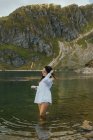 Усміхнена красива жінка стоїть в озері в схилі пагорбів і торкається волосся . — стокове фото
