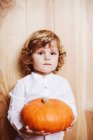 Pensive boy posing with pumpkin on wooden backdrop — Stock Photo
