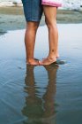 Section basse du couple debout en eau peu profonde à la plage — Photo de stock