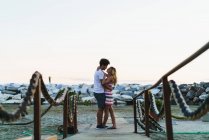 Side view of young people embracing romantically on coastline and looking at each other. — Stock Photo