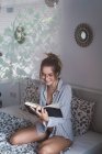 Smiling woman in eyeglasses reading book on bed — Stock Photo