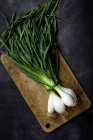 Still life of fresh onions on wooden board at dark table. — Stock Photo