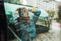 Выстрел через стекло молодая женщина позирует чувственно за стеклом автобусной остановки — стоковое фото