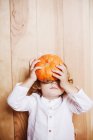 Child boy covering face with pumpkin on wooden backdrop — Stock Photo