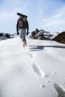 Back view of man with backpack walking in snowy mountains in sunlight. — Stock Photo