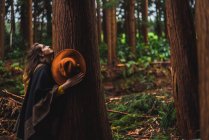 Вид збоку чуттєвої жінки, що обіймає старе дерево в лісі . — стокове фото