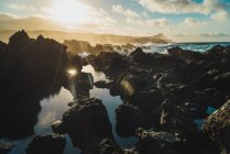Vue panoramique sur les roches sombres dans les lumières du coucher du soleil au bord de la mer . — Photo de stock