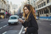 Вид сбоку симпатичной женщины, стоящей на улице и просматривающей смартфон . — стоковое фото