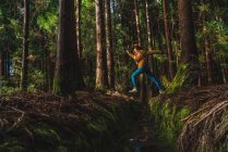 Вид сбоку на молодую женщину, прыгающую через канаву в лесу — стоковое фото