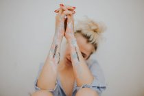 Pretty blonde woman with painted and tattooed arms at gray wall. — Stock Photo