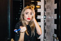 Mujer rubia triste posando con cepillo de dientes en el baño - foto de stock