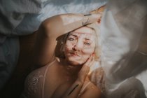 From above view of young woman lying on bed with curtain shadow on face. — Stock Photo