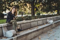 Женщина сидит на каменной скамейке и читает книгу в парке — стоковое фото