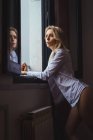 Mulher atraente na camisa encostada à janela — Fotografia de Stock