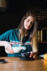 Брюнетка сидит за столом и наливает молоко в чашку — стоковое фото