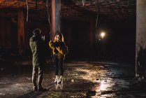 Visão traseira do fotógrafo atirando mulher com tocha de iluminação no prédio abandonado — Fotografia de Stock