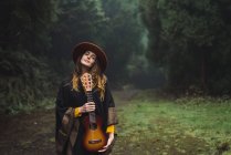 Mulher encantadora posando com ukulele em bosques nebulosos — Fotografia de Stock