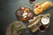 Dall'alto spuntini di carne saporiti con pane e verdure su piatti di pietra . — Foto stock