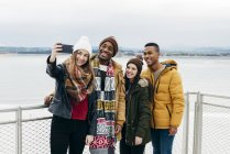 Alegre amigos multirraciais em pé no porto e tomar selfie juntos . — Fotografia de Stock