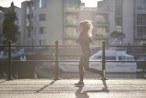 Вид сбоку на женщину, бегущую по улице на закате — стоковое фото