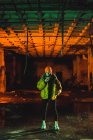 Молодая стильная женщина в желтой куртке стоит и использует смартфон в грязном заброшенном здании . — стоковое фото