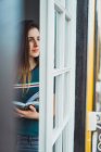 Sonhando menina com livro em mãos olhando para longe na janela — Fotografia de Stock