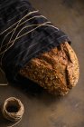 Vue rapprochée du pain fraîchement cuit enveloppé dans une serviette et serrer avec une bobine de fil sur fond sombre — Photo de stock