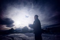 Mann fliegt Drohne mit Fernbedienung in verschneiter Landschaft. — Stockfoto