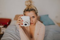 Молода жінка з миттєвою камерою сидить на ліжку . — стокове фото