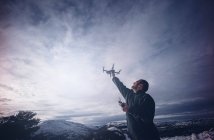 Mann versucht fliegende Drohne in verschneiter Landschaft zu erwischen. — Stockfoto