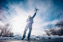 Mann greift in verschneiter Landschaft nach fliegender Drohne. — Stockfoto