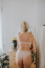 Visão traseira da mulher loira em lingerie em pé no espelho em casa . — Fotografia de Stock