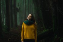 Женщина в желтом свитере смотрит вверх в лесу — стоковое фото